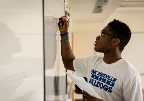 Economics student working on a problem at a white board